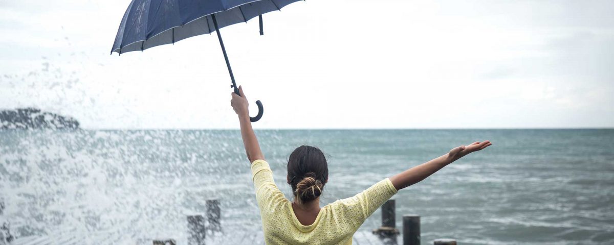 Mom sitting on a warf looking at the sea with an umbrella in one hand and other hand outstretched