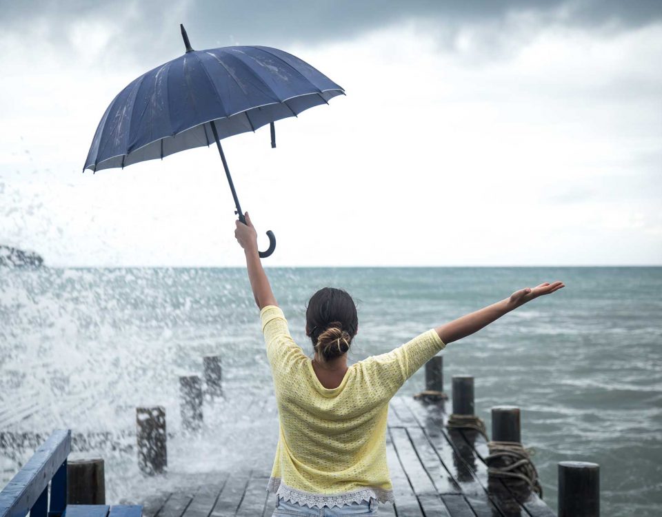 Mom sitting on a warf looking at the sea with an umbrella in one hand and other hand outstretched