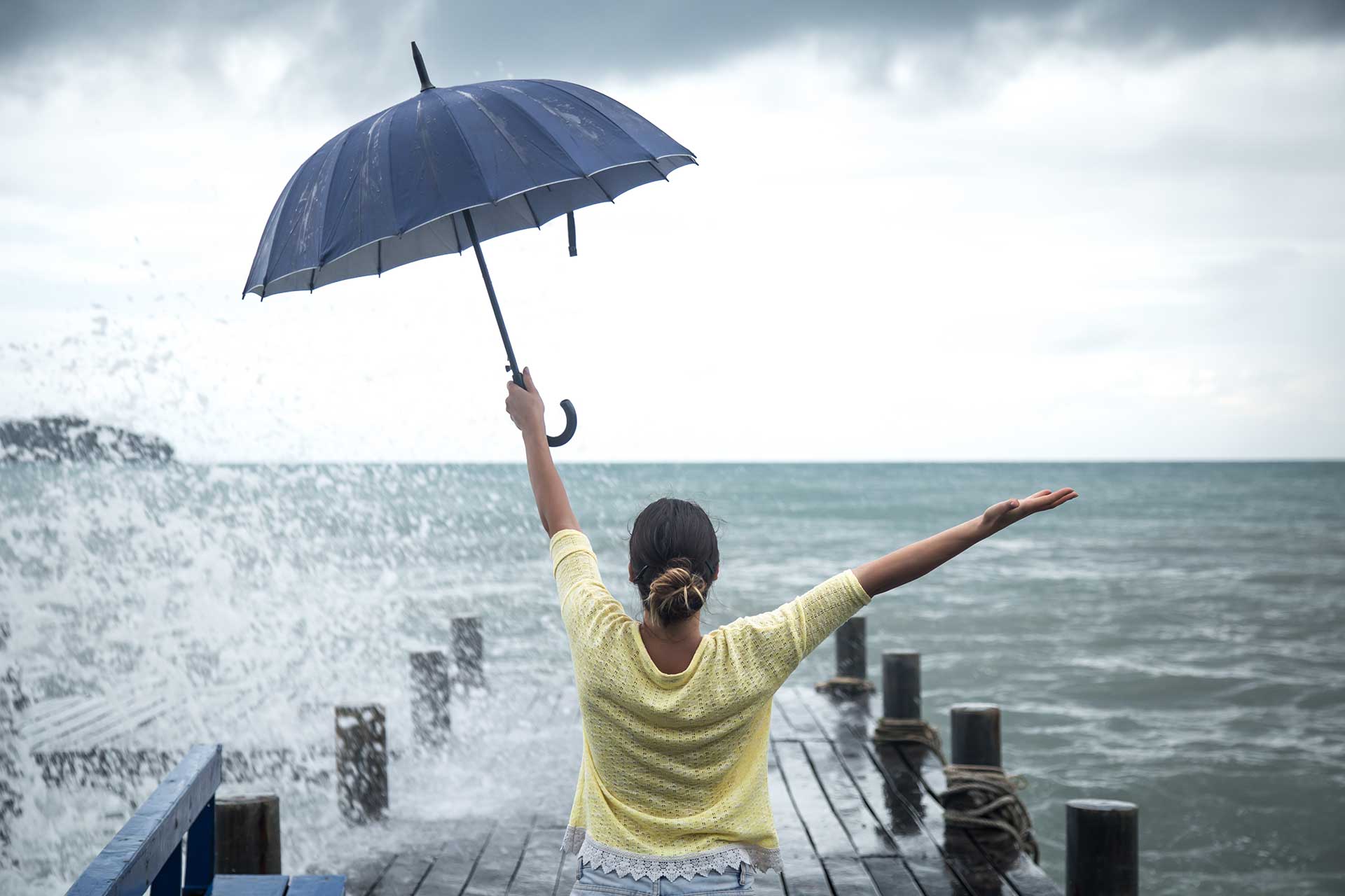 Mom sitting on a warf looking at the sea with an umbrella in one hand and other hand outstretched